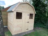 Dutch Barn shed with gambrel roof, single door and two front windows, natural timber on paving