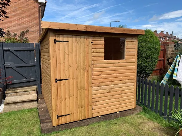 Classic pent timber shed with single door and window in residential garden