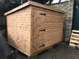 Natural timber pent shed with single door and strap hinges on raised base
