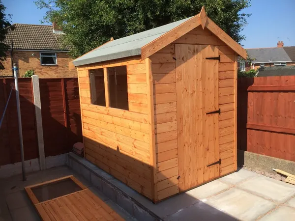 Natural timber apex garden shed with single door and side windows on paved patio