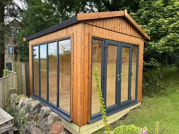 Modern Apex Garden Room from an angle showing full-height side glazing and natural timber cladding in a garden setting