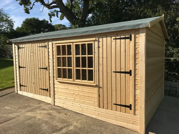 Dark green apex workshop with row of opening windows and single door in a rural setting