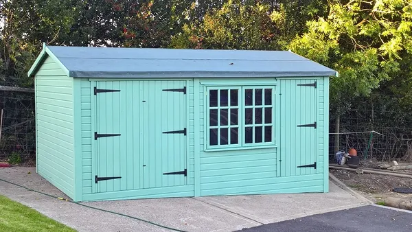 Natural timber apex workshop with two sets of double doors and central multi-pane window on paved base