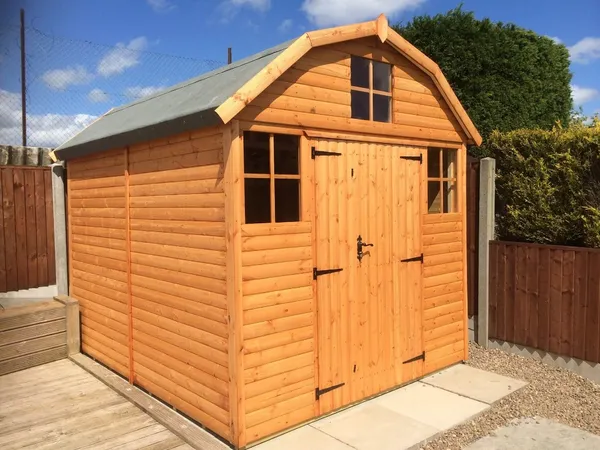 Dutch Barn shed with traditional gambrel roof and pink roses, classic country garden setting