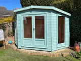 The Haven Corner Summerhouse in light blue with white trim and composite decking