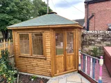 The Haven Corner Summerhouse in light grey with top-hung opening sashes on stone patio