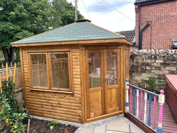The Haven Corner Summerhouse in light grey with top-hung opening sashes on stone patio