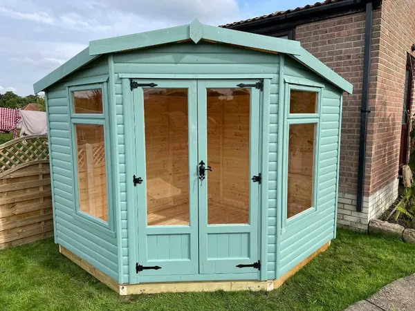 The Haven Corner Summerhouse in teal with panoramic glazing on paved base