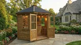 The Panoramic Octagon Summerhouse configured as a home bar on flagstone patio with open double doors, bar counter, shelving and string lights in a landscaped garden