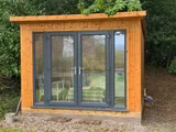 The Modern Pent Garden Room front view with dark fascia, panoramic glazing and gravel approach