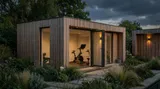 The Pentrich Garden Room with vertical slatted cedar and bi-fold doors, used as a home gym with exercise equipment, moody evening lighting