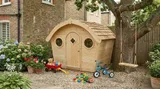 Curved-roof playhouse in natural timber with wooden shingles and circular porthole windows