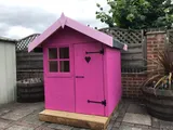 Vibrant pink playhouse with apex roof, 4-pane window and heart cutout in door