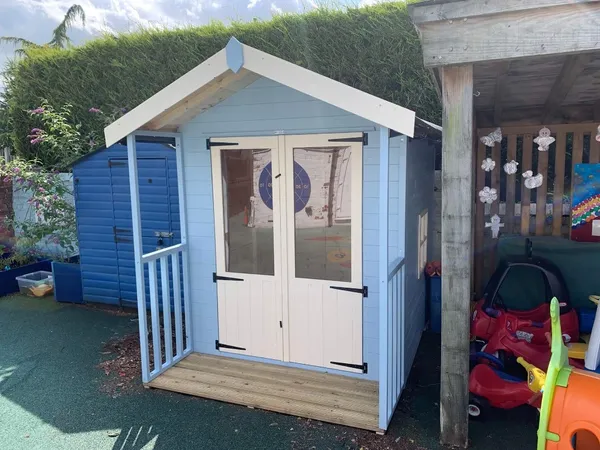 Pale blue playhouse with integrated front veranda, safety railings and double doors