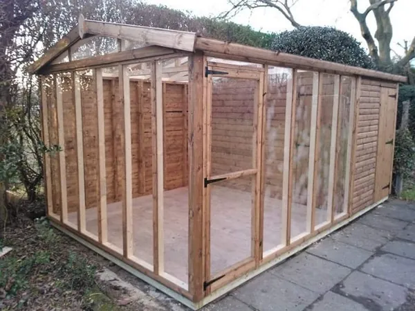 Exterior view of a honey-brown timber potting shed featuring large double doors with heavy-duty galvanized hinges and a sloping glass wall for maximum natural light