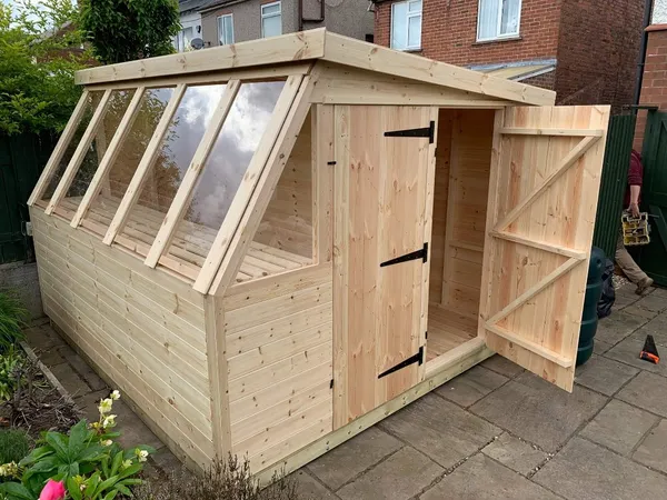 Natural timber potting shed with angled glazed roof and door ajar, shelving visible inside