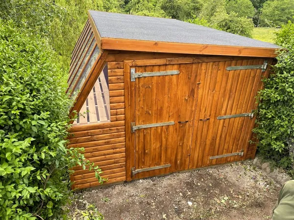 Exterior view of a premium timber potting shed with an apex roof, featuring double glazed doors, a side entrance, and an open roof vent on a stone patio