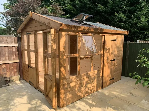 Exterior view of a large timber potting shed featuring extensive floor-to-ceiling glazing on two sides and a separate integrated storage section with a solid door
