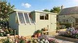 Sage green potting shed with integrated greenhouse section and workspace in a landscaped garden